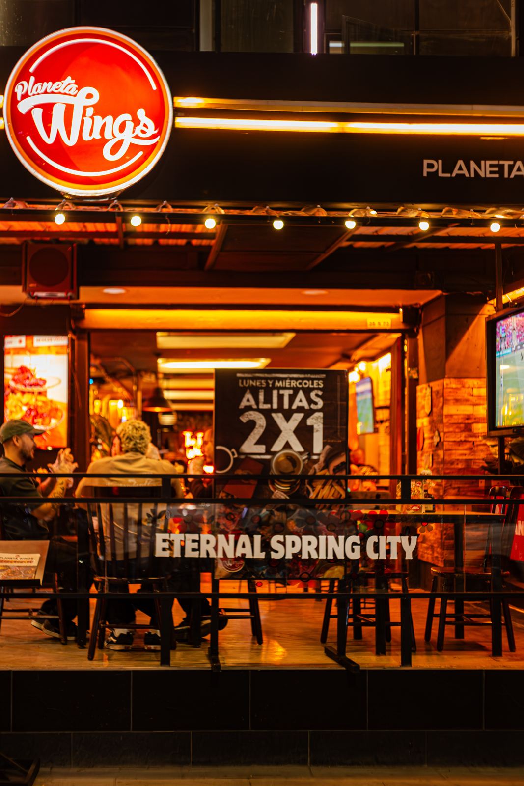 Fachada de Planeta Wings Laureles de noche, con el aviso de alitas 2x1